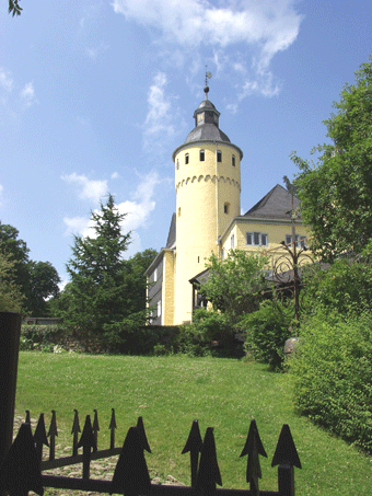 Das Foto zeigt eine Ansicht von Schloss Homburg mit dem Schlossturm im Hintergrund und deinem Teil des Garten im Vordergrund