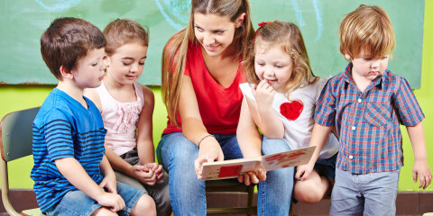 Kinder mit Erzieher lesen Buch im Kindergarten