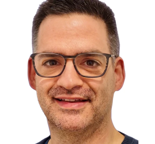 Porträt eines Mannes mit kurz geschnittenem Haar, Brille und einem dunkelblauen Pullover vor weißem Hintergrund.