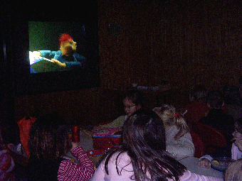 Das Foto zeigt den abgedunkelten Raum, in dem der Film zum Thema Zahngesundheit vorgeführt wird mit einem Blick auf die Leinwand