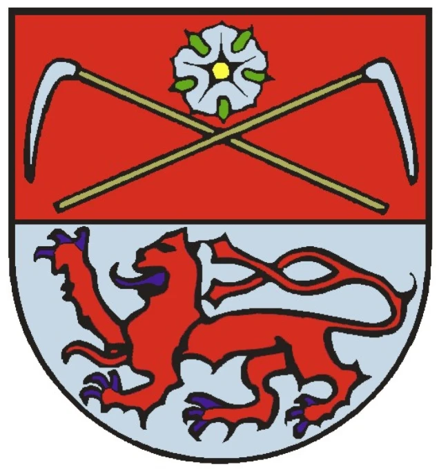 Ein Wappen mit einem roten oberen Feld, darin zwei gekreuzte Sensen und eine weiße Blume mit grünem Blattwerk. Im unteren silbernen Feld ein roter Löwe.