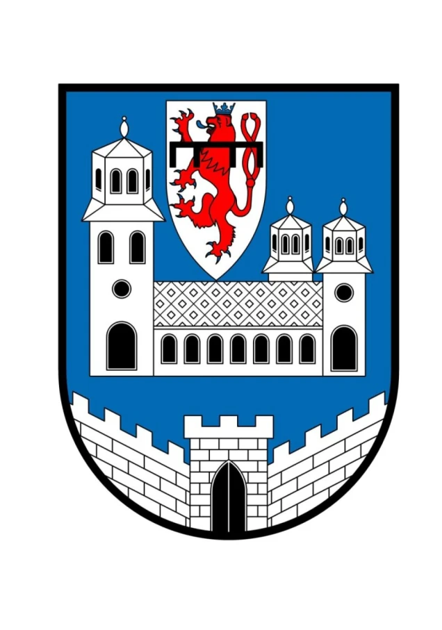 Ein Wappen mit blauem Hintergrund zeigt eine weiße Burg mit drei Türmen und einer Mauer mit Tor. Oben in der Mitte ist ein roter, gekrönter Löwe auf weißem Schild abgebildet.