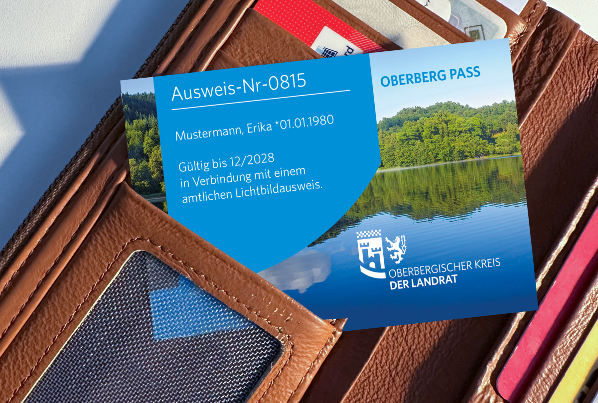 Eine braune Geldbörse mit einer Karte darin, die als 'Oberberg Pass' gekennzeichnet ist. Die Karte zeigt eine Landschaft mit Wald und See.