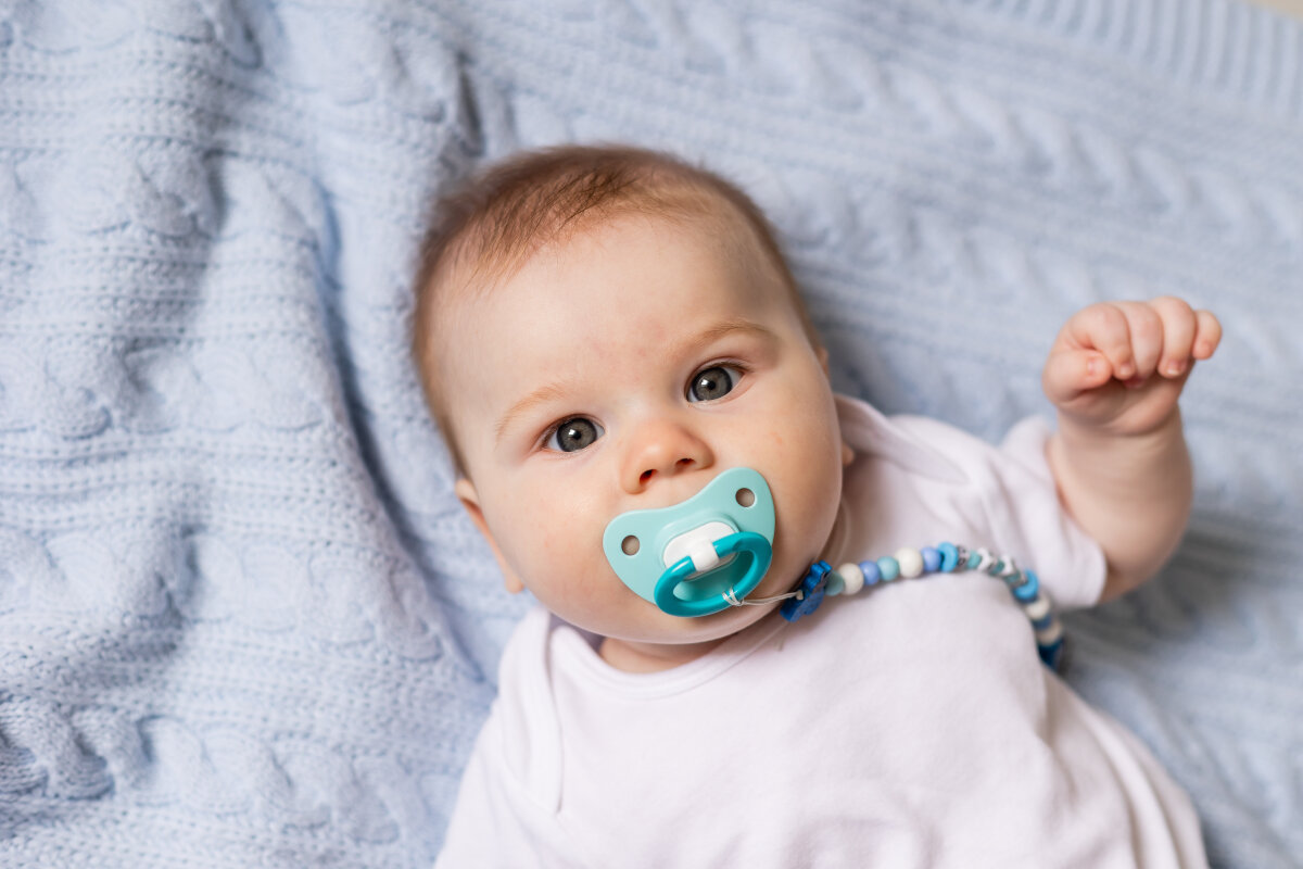 portrait of cute newborn baby with a pacifier in his mouth lying on his back on blue knitted blanket