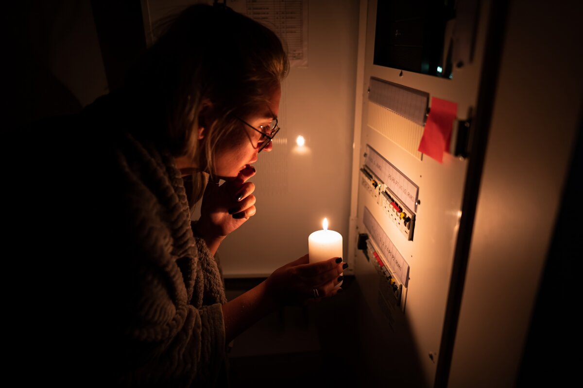 A girl is checking an electrical shield after an electrical blackout. Using a candle in the dark trying to figure out what happened. Electrical malfunction.