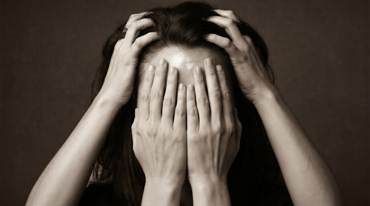 Eine Person hält sich mit zwei Händen den Kopf, während zwei andere Hände das Gesicht bedecken. Der Hintergrund ist dunkel und einfarbig.