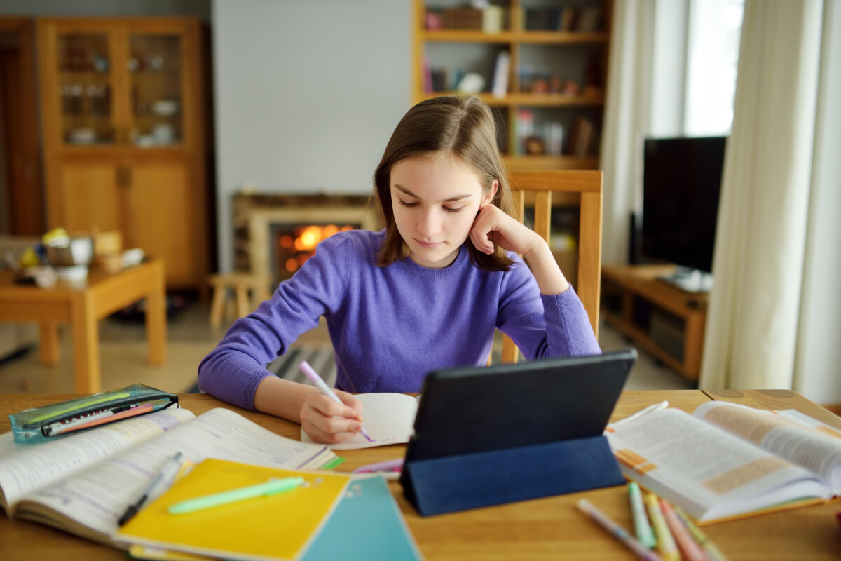 Preteen schoolgirl doing her homework with digital tablet at home. Child using gadgets to study. Education and distance learning for kids. Homeschooling during quarantine.