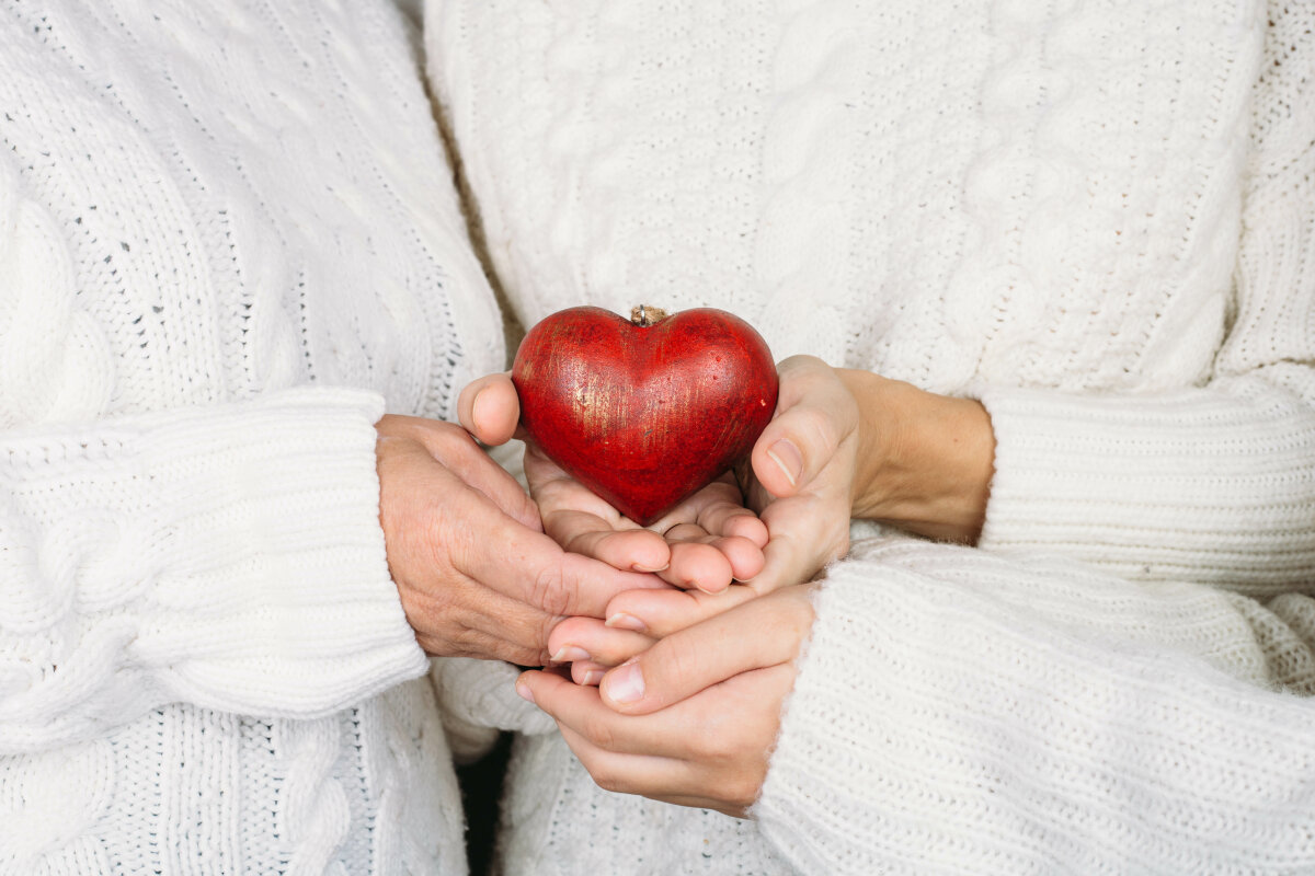 three womans holding red heart in hands.  Love concept to Valentine's Day . Women of different ages in warm sweaters hold a wooden heart