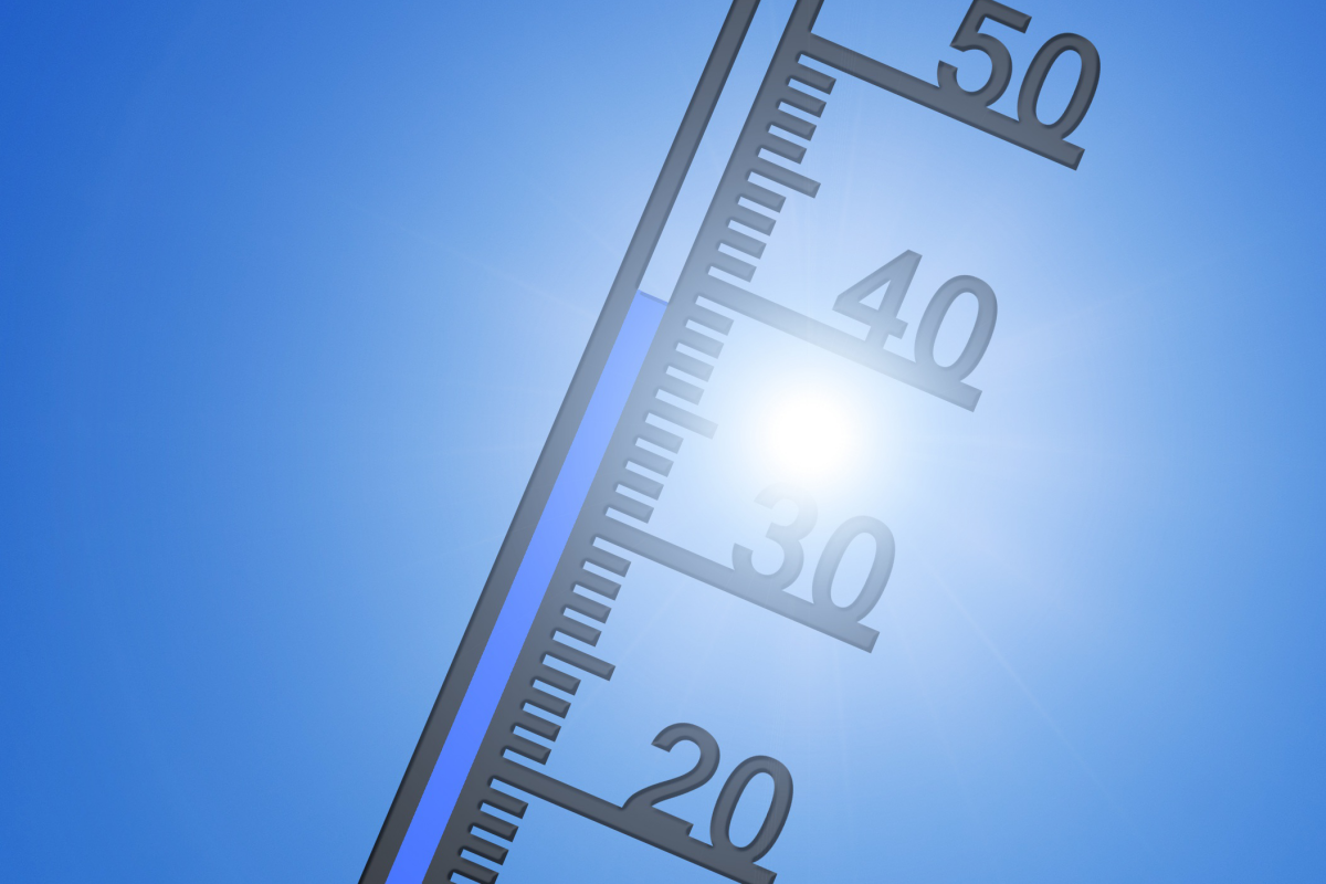 Ein Thermometer mit einer Skala, die Temperaturen bis 50 Grad Celsius anzeigt, vor einem klaren blauen Himmel und einer strahlenden Sonne.