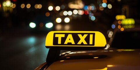 Leuchtendes gelbes Taxi-Schild auf einem Fahrzeugdach, nachts aufgenommen mit unscharfen Lichtern und Verkehr im Hintergrund.