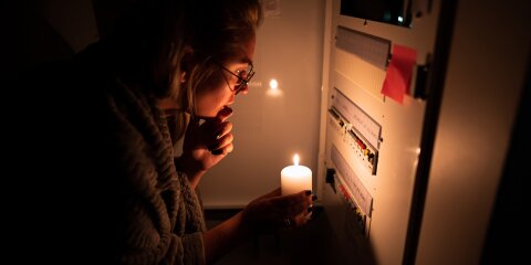 A girl is checking an electrical shield after an electrical blackout. Using a candle in the dark trying to figure out what happened. Electrical malfunction.