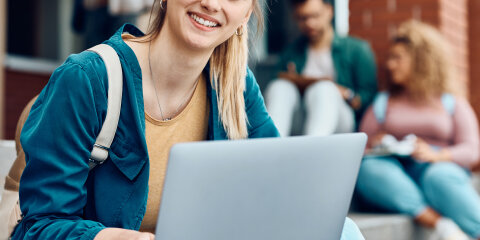 Happy female student using laptop at campus and looking at camera.