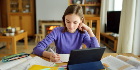 Preteen schoolgirl doing her homework with digital tablet at home. Child using gadgets to study. Education and distance learning for kids. Homeschooling during quarantine.