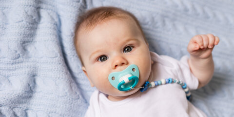 portrait of cute newborn baby with a pacifier in his mouth lying on his back on blue knitted blanket
