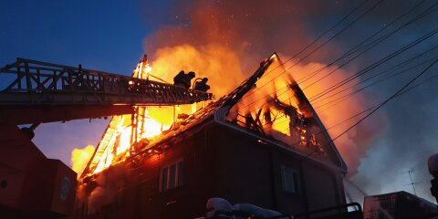 The roof of the house is on fire. The residential building burn, village. Firefighters put out a fire from the crane from above. Smoke and sparks.