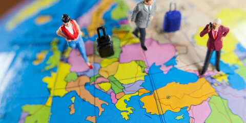 Miniaturfiguren von Reisenden stehen auf einer Karte Europas. Die Figuren sind mit Koffern ausgestattet und in verschiedenen Farben gekleidet.