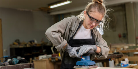 Portrait of a female carpenter using tools for making furniture in a furniture factory. with modern tools