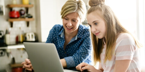 A mother using a laptop in kitchen with teenager