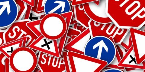 Ein Stapel verschiedener Verkehrsschilder, darunter Stoppschilder, Vorfahrt gewähren, Verbotsschilder und Richtungspfeile in verschiedenen Formen und Farben.