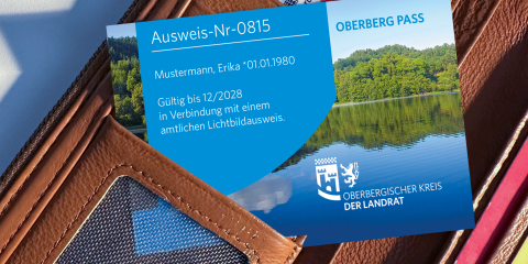 Eine braune Geldbörse mit einer Karte darin, die als 'Oberberg Pass' gekennzeichnet ist. Die Karte zeigt eine Landschaft mit Wald und See.