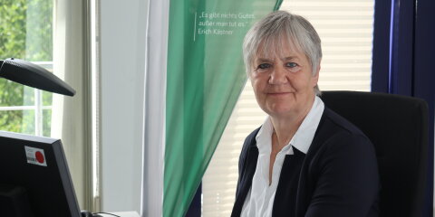 Eine Person sitzt an einem Schreibtisch mit Tastatur und Monitor. Im Hintergrund steht ein Banner mit der Aufschrift 'Ehrenamtsinitiative Weitblick Oberbergischer Kreis'.