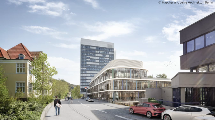 Städtische Straßenszene mit modernen und historischen Gebäuden. Im Vordergrund parken Autos, eine Person geht auf dem Gehweg, und im Hintergrund ist ein hoher Bürokomplex zu sehen.