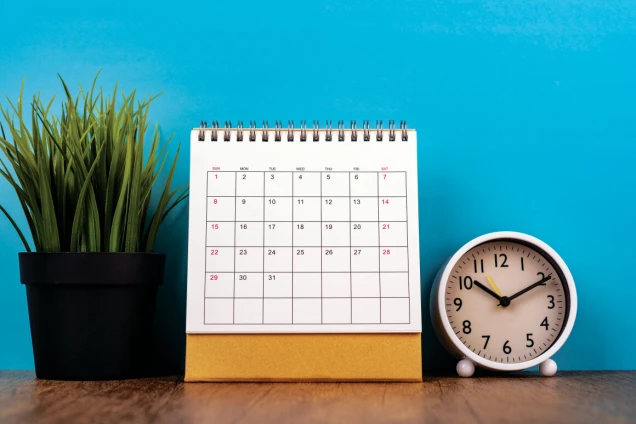 March 2026 desk calendar with clock and potted grass on wooden table. Blue background, time management, and spring planning concept.