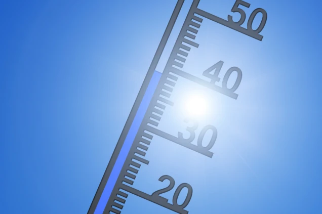 Ein Thermometer mit einer Skala, die Temperaturen bis 50 Grad Celsius anzeigt, vor einem klaren blauen Himmel und einer strahlenden Sonne.