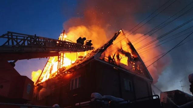 The roof of the house is on fire. The residential building burn, village. Firefighters put out a fire from the crane from above. Smoke and sparks.