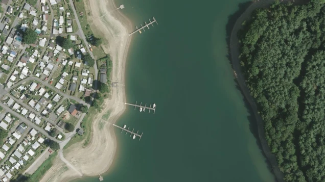 Luftaufnahme der Bevertalsperre mit Wohngebäuden links, mehreren Stegen mit Booten im Wasser in der Mitte und dichtem Wald rechts.