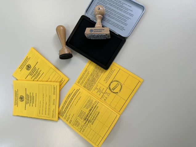 Gelbe Impfausweise und zwei Holzstempel mit Stempelkissen auf einer weißen Oberfläche.