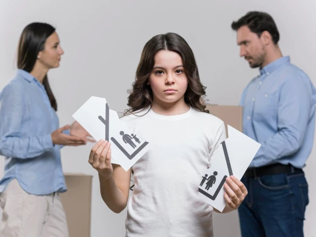 Kind steht im Vordergrung uns hat ein zerissenes Blatt in der Hand auf der einen zerrissenen Seite ist eine Haushälfte mit einem Kind und einem Vater und auf der anderen Seite eine Mutter und ein Kind. Im Hintergrund sieht man Eltern die links und rechts stehen. 
