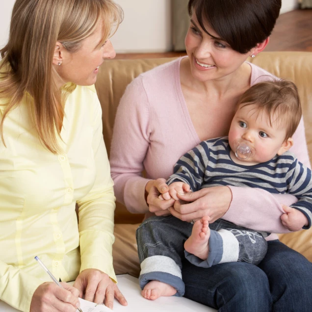 Mother With Baby Talking With Health Visitor At Home