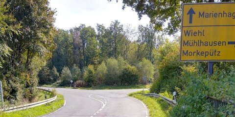Straßenkreuzung mit Beschilderung. Gelbes Schild zeigt Richtungen nach Marienhagen, Wiehl, Mühlhausen und Morkepütz. Umgeben von grüner Vegetation und Bäumen.