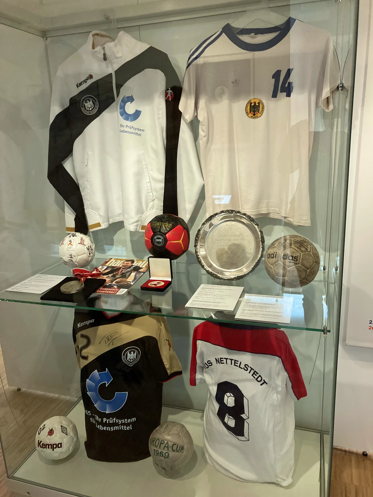 Weltmeisterliches aus dem Oberbergischen Kreis: das Trikot von Heiner Brand aus dem Jahr seines ersten Weltmeistertitels 1978 und (u.a.) die Trophäe von Gummersbachs erster Meisterschaft 1966. (Foto: OBK) 