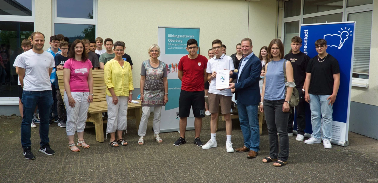 Das Bildungsbüro Oberberg, vertreten durch Anke Koester, die Leiterin des Amtes für Schule und Bildung und die AggerEnergie haben offiziell den Hauptpreis der Verlosung anlässlich des Bundesweiten Vorlesetages 2021 an das Wüllenweber-Gymnasium (WWG) Bergneustadt übergeben. Karim, Schüler am WWG, hat die Heißluftballonfahrt gewonnen und bekommt den Gutschein vom Leiter Unternehmenskommunikation der AggerEnergie Peter Lenz überreicht.(Foto: OBK)