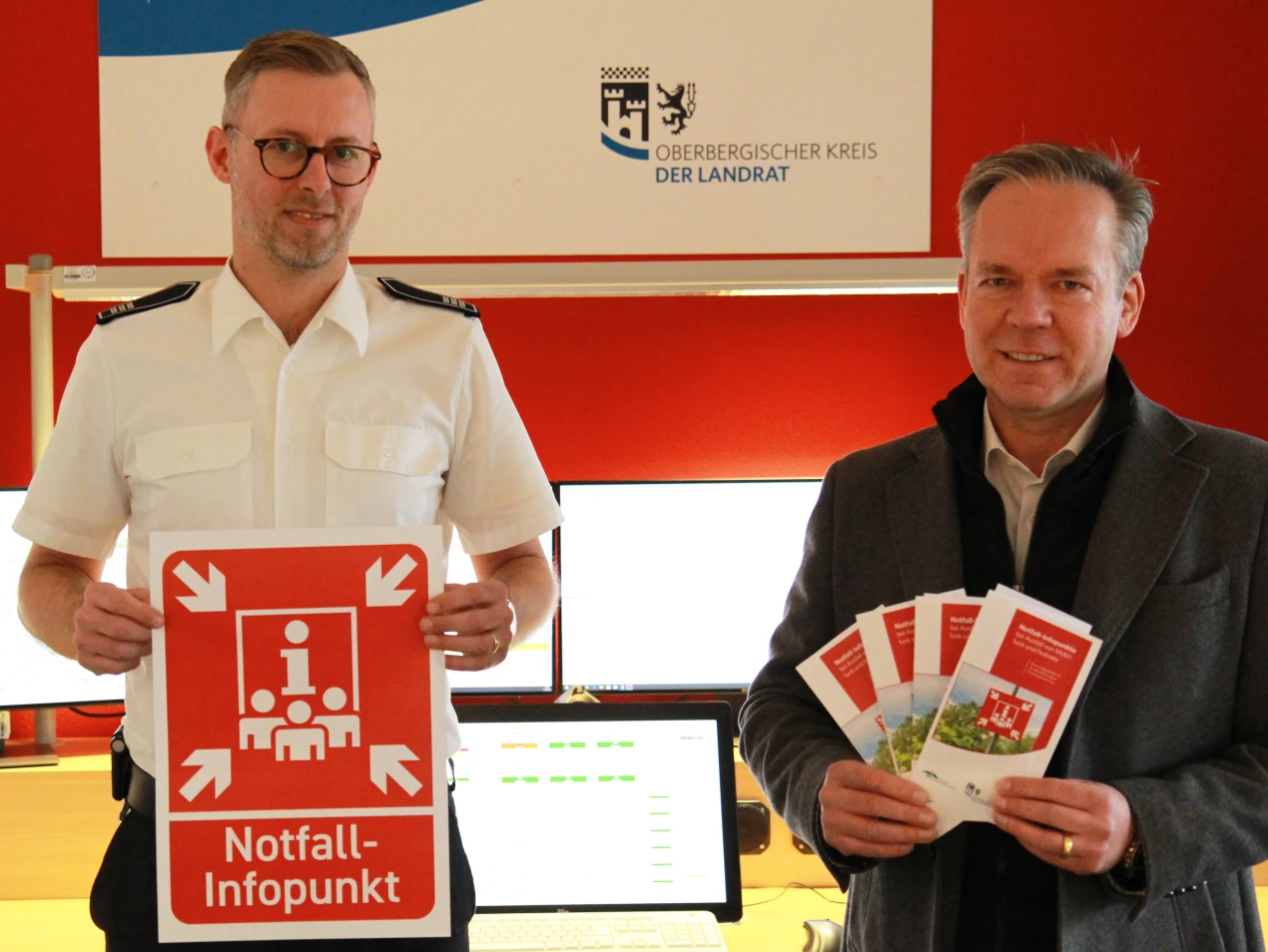 Julian Seeger (Leiter Feuer- und Rettungsleitstelle Oberbergischer Kreis, l.) und Kreisdirektor Klaus Grootens (r.) zeigen die Flyer und die geplanten Hinweisschilder für die Notfall-Infopunkte. (Foto: OBK)