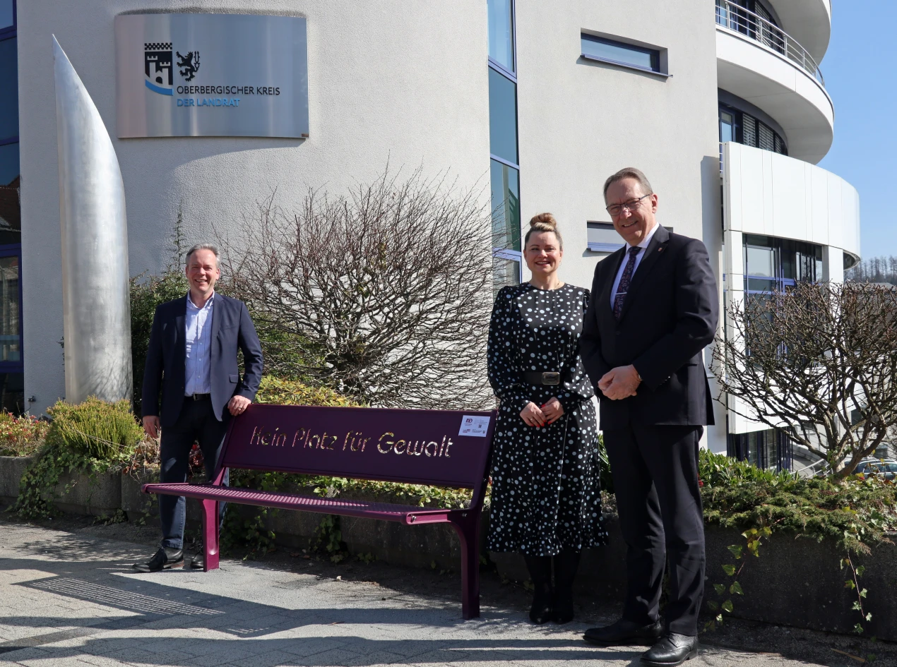 Landrat Jochen Hagt (r.), Kreisdirektor Klaus Grootens und die Gleichstellungsbeauftragte des Oberbergischen Kreises, Magdalena Tertel, weisen auf die Motivbank "Kein Platz für Gewalt" am Haupteingang des Kreishauses hin. (Foto: OBK)   