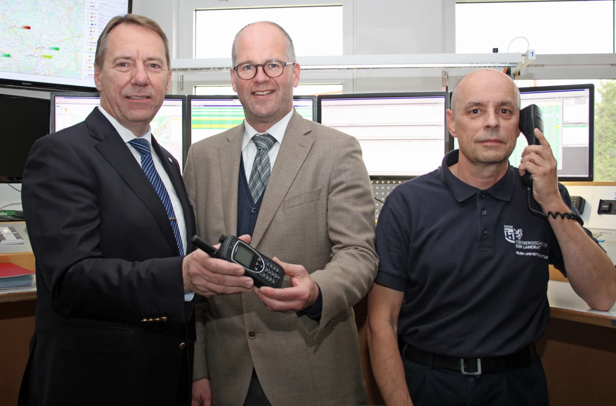 Kleines Gerät mit modernster Technik: Landrat Jochen Hagt (l.) und Bernhard Kiesecker, Leiter der Kreisleitstelle (r.) erhalten das neue Satellitentelefon von AggerEnergie-Chef Frank Röttger (Foto:OBK).