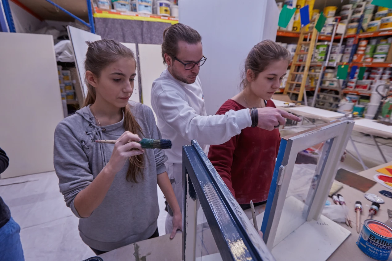 Maximillian Janscheidt (Mitte) von der Firma Bondke zeigt Sofia Girenko (l.)und Fabiena Rugovaj(r.)wie „Läufer“ beim Lackieren des Fensters vermieden werden können. (Foto: OBK)