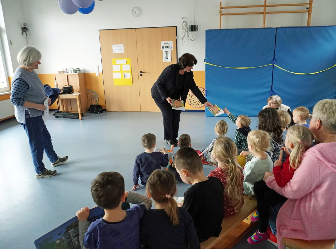 Freude bei Kitaleiterin Bettina Dörpinghaus und den Kita-Kindern: Birgit Steuer, die Leiterin des Bildungsbüros des Oberbergischen Kreises, übergibt den Kindern das Comicbuch des Bildungsbüros für die Kita-Bibliothek der Kath. Kindertagesstätte St.Raphael. (Foto: OBK) 