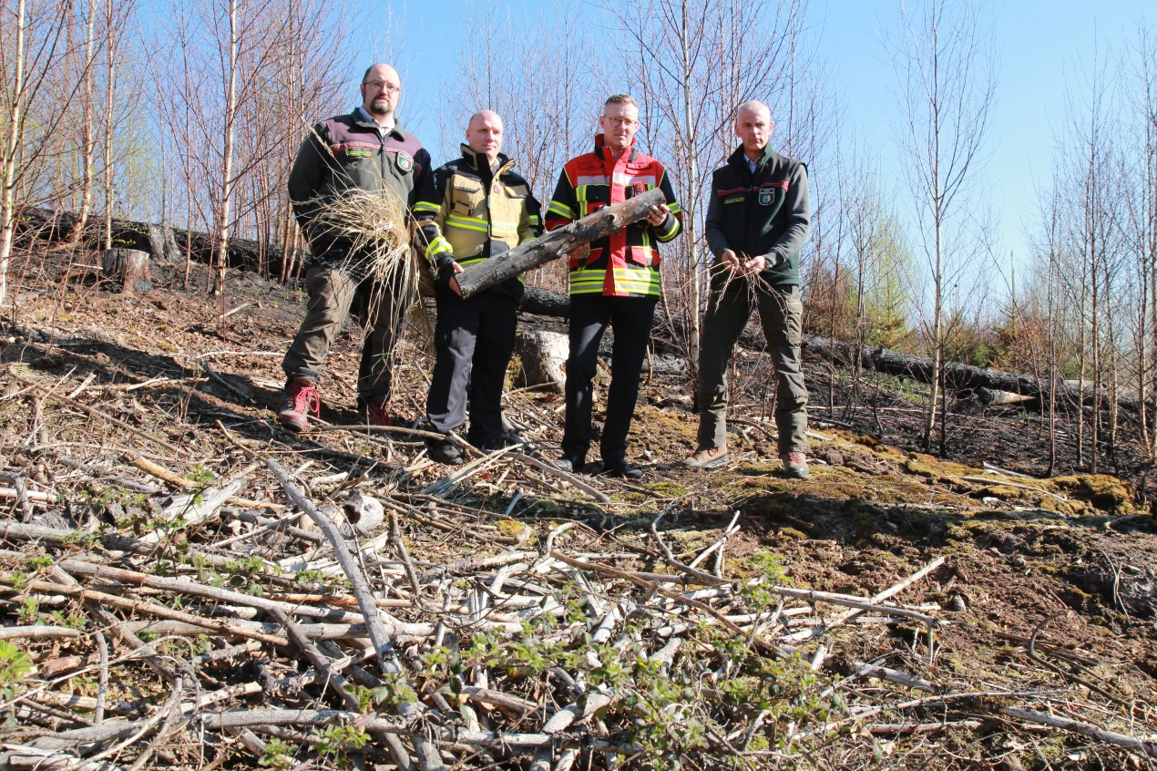 Stefan Wende (Feuerwehrfachberater Forst des Regionalforstamtes Bergisches Land), Manuel Packhäuser (KBM Rheinisch-Bergischer Kreis), Julian Seeger (KBM Oberbergicher Kreis) und Leiter des Regionalforstamtes Bergisches Land) zeigen die erhöhte Brandlast vor der verbrannten Fläche. (Foto: OBK)