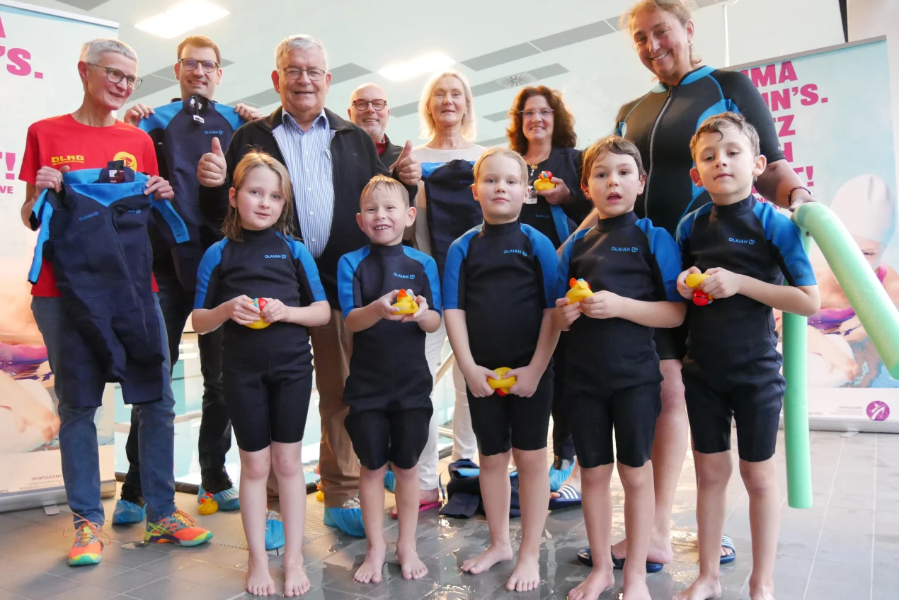 Freuen sich, dass die Neoprenanzüge jetzt im Schwimmunterricht von den Kindern genutzt werden (v.l.): Henrike Schreyer-Vogt, 2. Vors. des DLRG Engelskirchen e.V.; Tim Vogel, Geschäftsführer des Stadtsportverband Wiehl; Hagen Jobi, Vorsitzender des Kreissportbund Oberberg e.V.; Hartmut Livreé, 1. Vors. des Stadtsportverband Wiehl; Anja Lepperhoff, Geschäftsführerin des Kreissportbund Oberberg e.V.; Birgit Steuer, Leiterin der Koordinierungsstelle Gesellschaftliche Entwicklung des Oberbergischen Kreises und Ellen Vleer, 1. Vors. des Wiehler Schwimmvereins mit den Nachwuchsschwimmern Kathleen, Liam, Finn, Paul und Rafael. (Foto: OBK)   