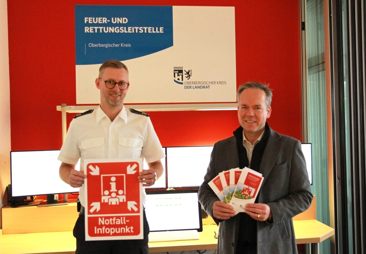 Die Notfall-Infopunkte werden beschildert. Flyer werden in den Kommunen und auf der Internetseite des Oberbergischen Kreises bereitgestellt. Julian Seeger (Leiter Feuer- und Rettungsleitstelle Oberbergischer Kreis, l.) und Kreisdirektor Klaus Grootens (r.) präsentieren Schild und Flyer. (Foto: OBK)